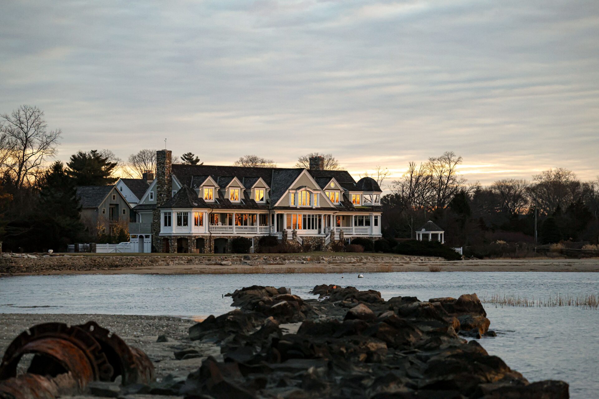 Waterfront shingle-style home with illuminated windows at dusk
